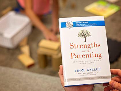 Person holding Strengths Based Parenting, with a child in the background.